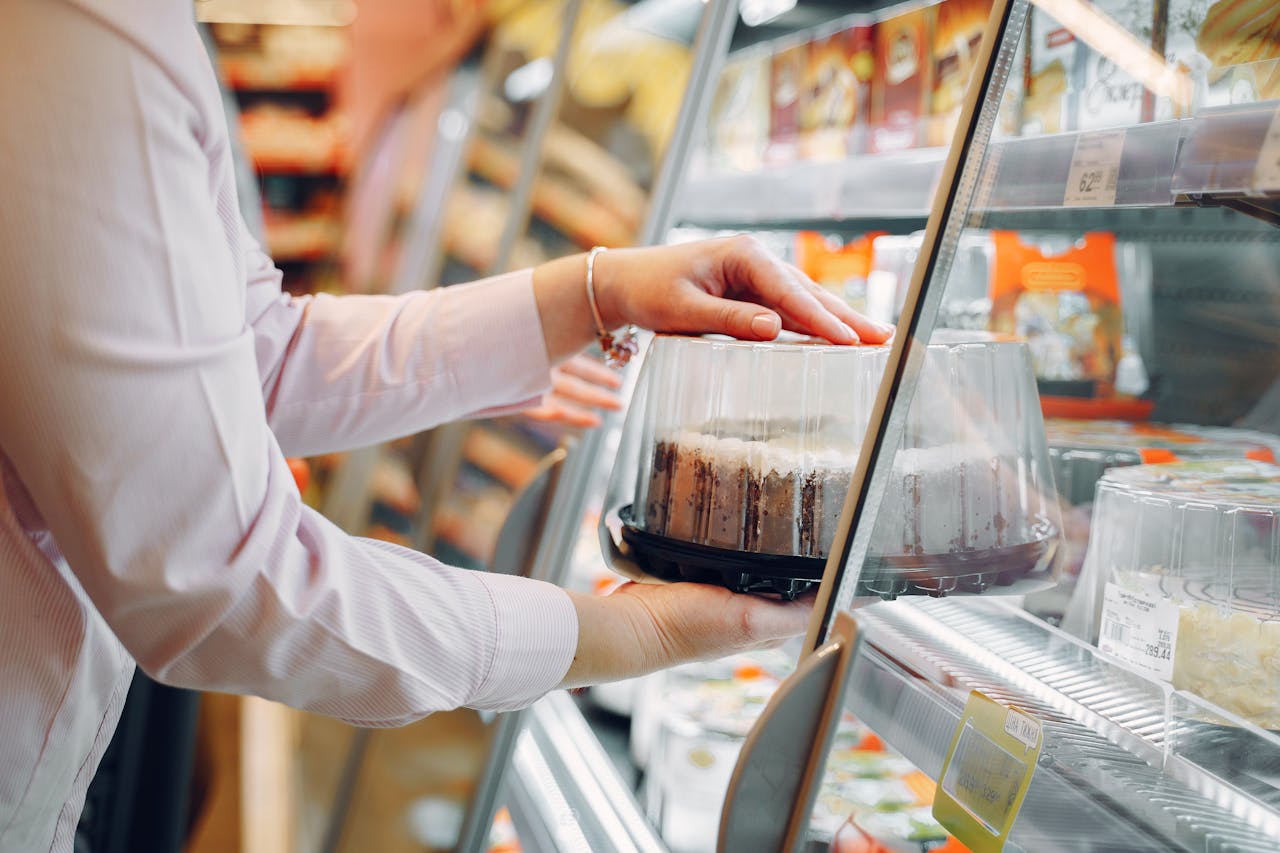 A woman choosing a packaged cake from a supermarket chiller.