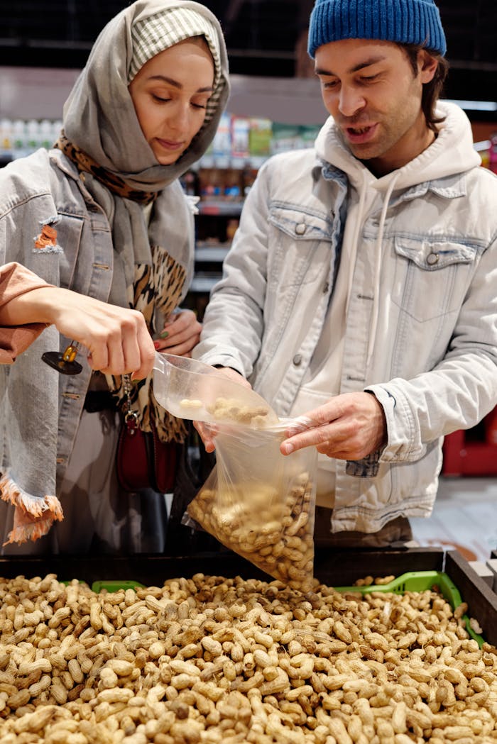 Middle Eastern couple selecting peanuts in a supermarket aisle, adding them into a bag.