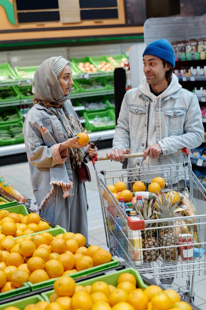 Home A man and woman in hijab shopping for oranges in a supermarket aisle.