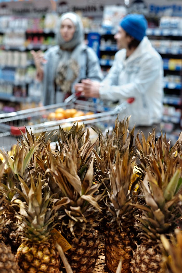 Two shoppers engaging in conversation near pineapples in a bustling supermarket.