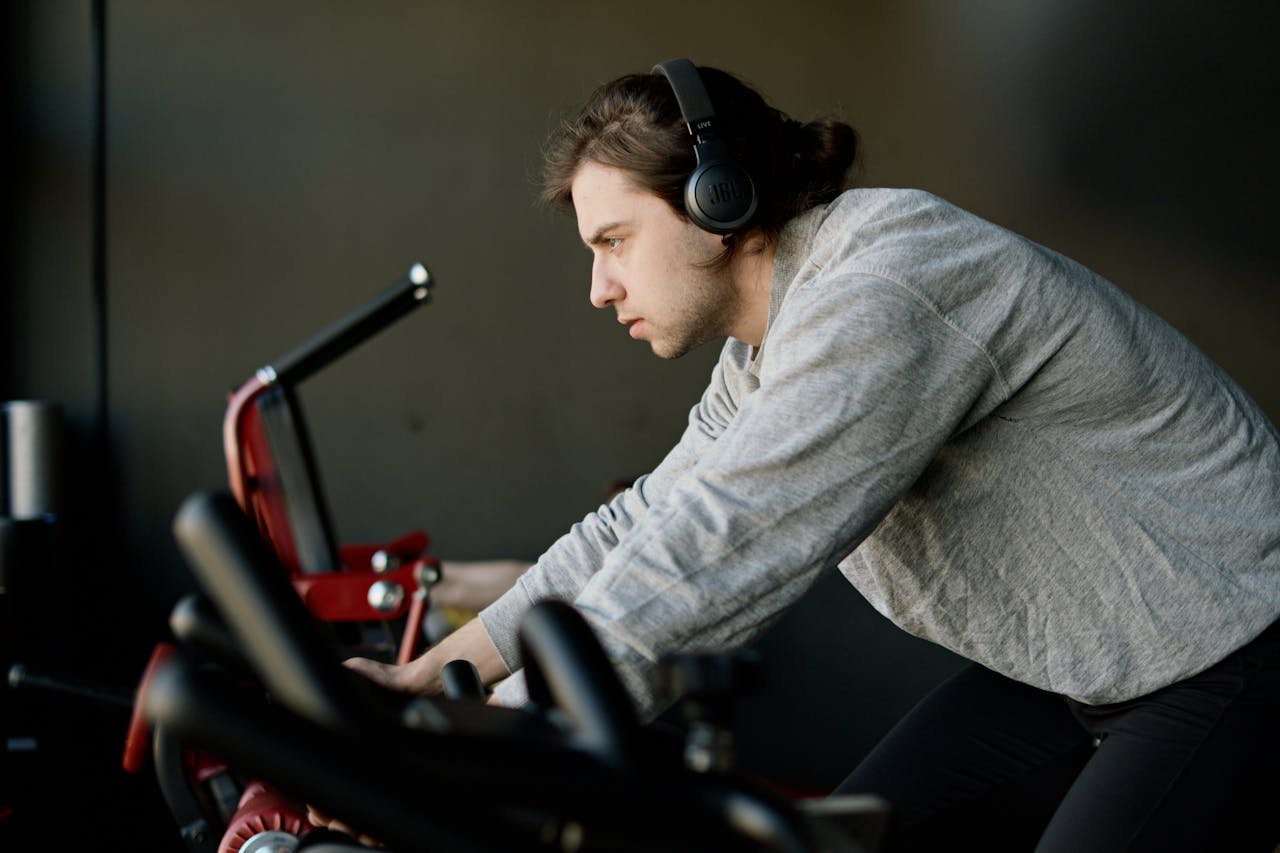 Determined young man training on exercise bike in gym, wearing headphones.