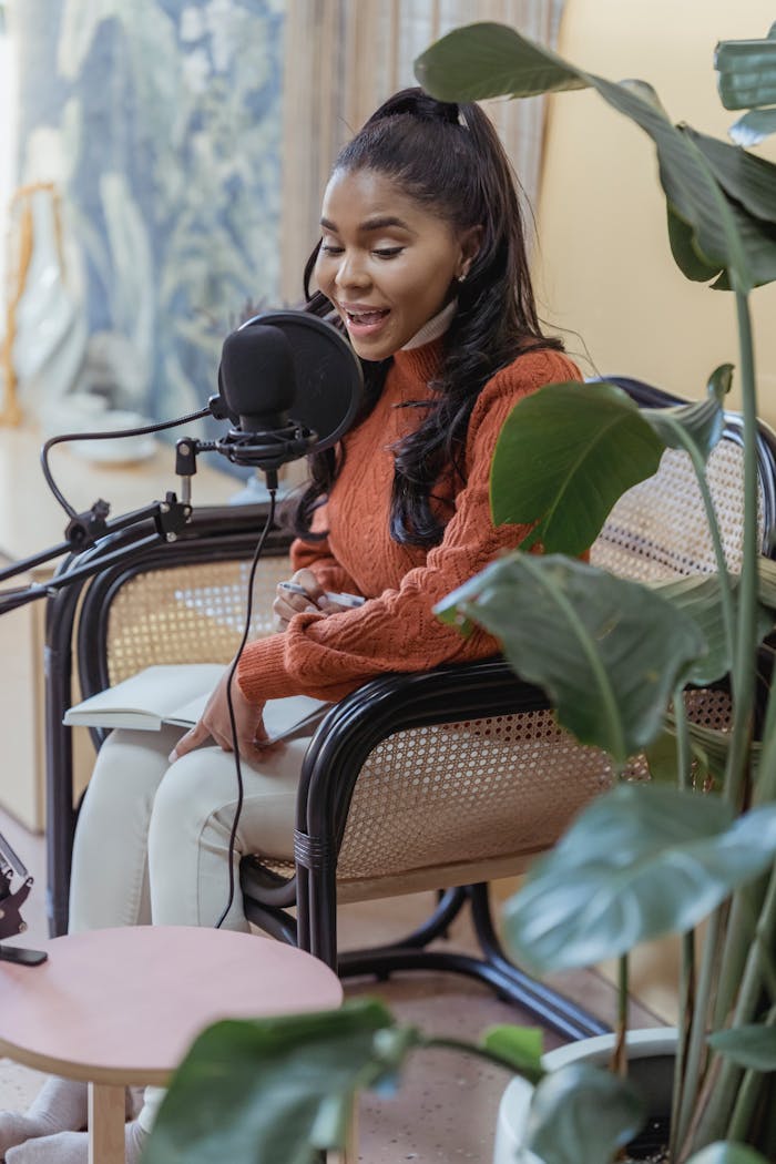 African American woman recording a podcast in an indoor studio with lush green plants.